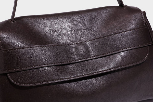 Strukturierte rechteckige dunkelbraune Schultertasche in Lederoptik mit Klappe, mehrlagigem Detail auf der Vorderseite und langem verstellbarem Riemen, Detailansicht