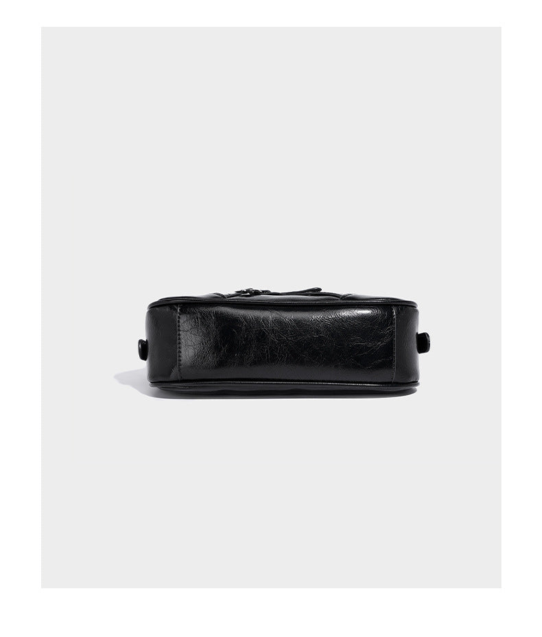 Compact moto-inspired shoulder bag with crisscross grommet strap detail, glossy textured finish, and adjustable crossbody