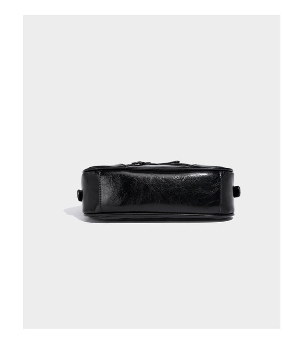 Compact moto-inspired shoulder bag with crisscross grommet strap detail, glossy textured finish, and adjustable crossbody