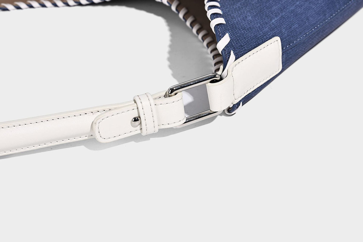 Denim-blue hobo tote with white leather-look shoulder strap, contrast whipstitch trim along curved open top, and silver-tone