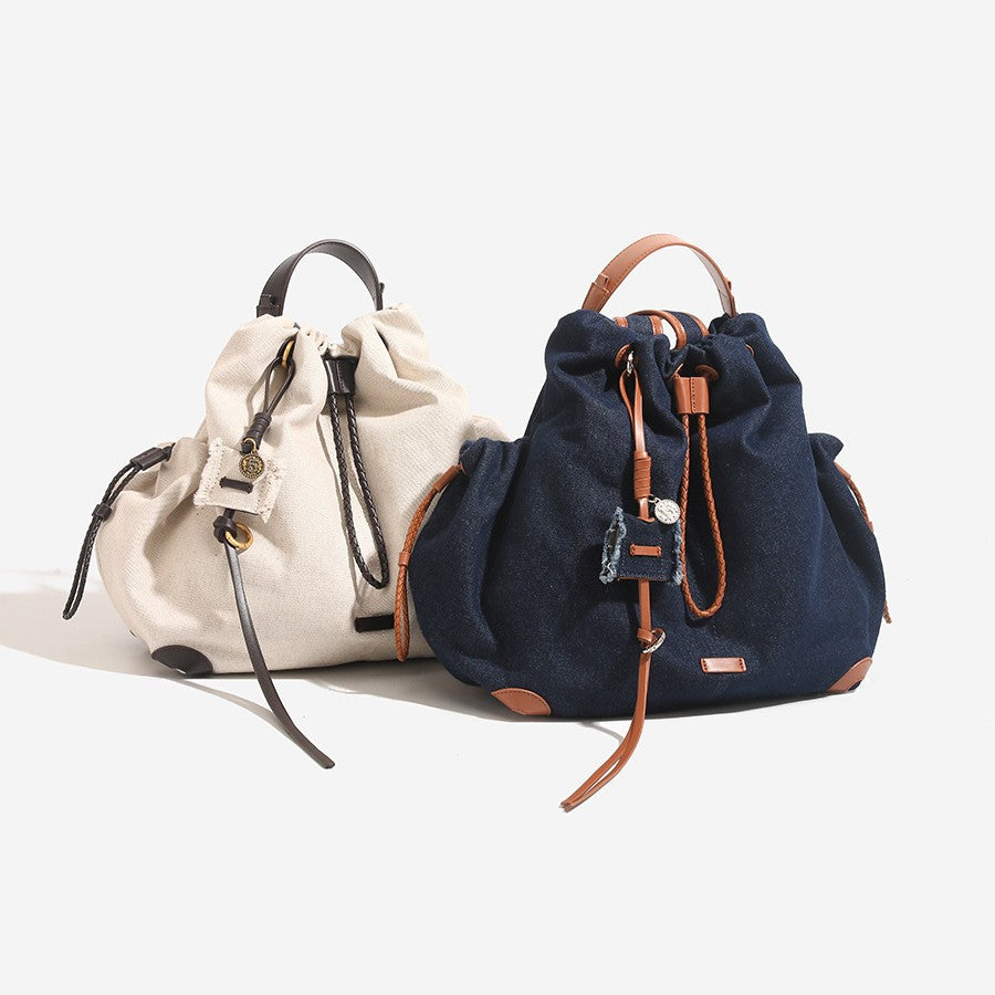 Slouchy drawstring bucket backpack with braided cord closure, tan leather-look trim and corner guards, detail view 2