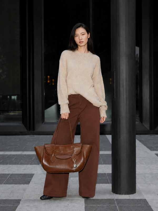 Large winged leather-look tote bag with single arched handle, stitched flap-front panel, and silver ball charm in cognac