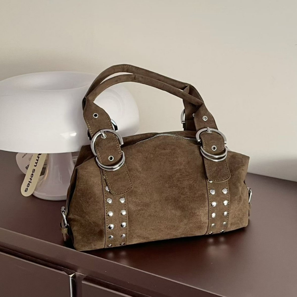 Matte suede-finish barrel bag with silver stud panels, oversized ring hardware, and dual top handles, front view