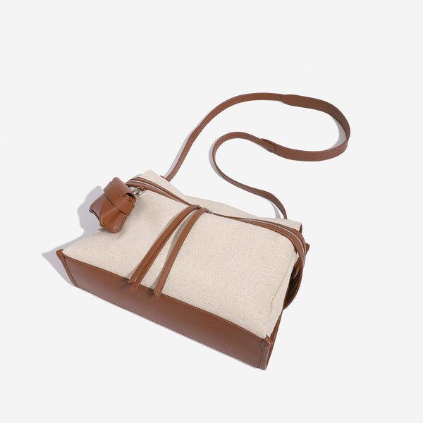 Cream canvas zip-top shoulder bag with cognac leather-look trim, dual zipper, attached mini pouch, and tassel strap ties