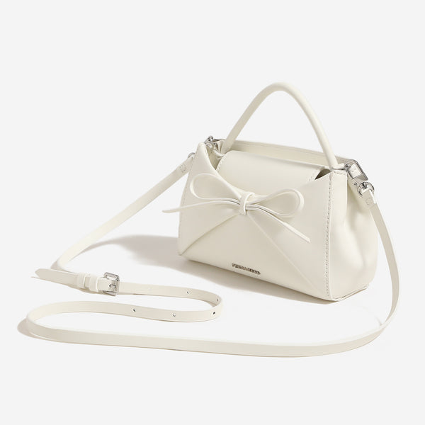 Structured mini trapezoid top-handle crossbody bag with sculpted bow front detail, smooth matte finish, silver-tone hardware