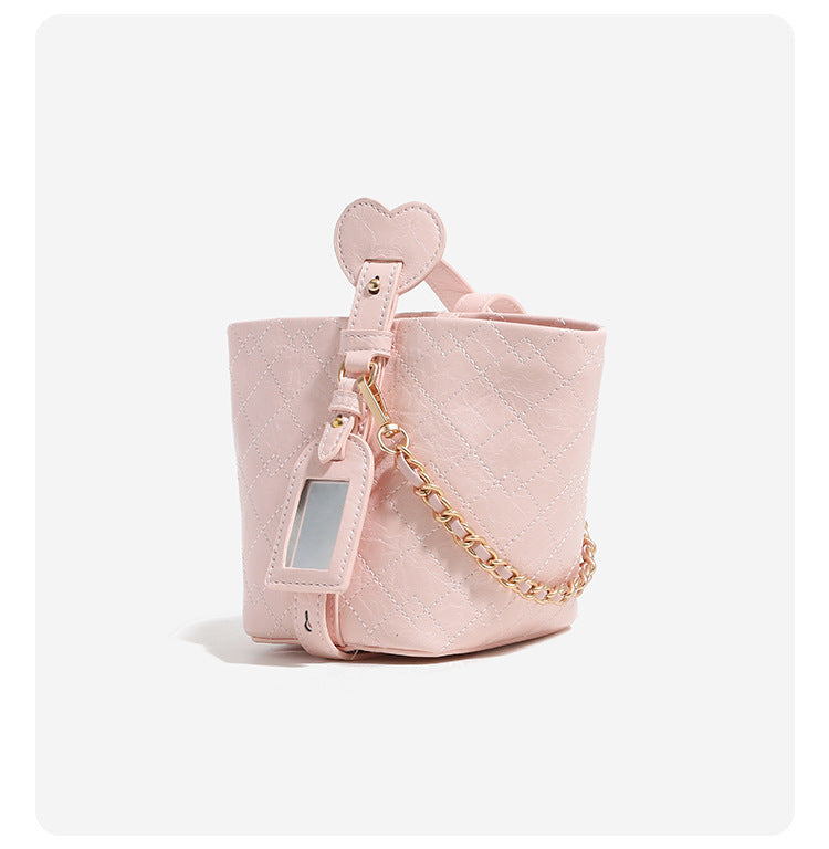 Small diamond-quilted bucket bag with gold-tone chain accent, heart strap detail, hanging tag, and matching zip coin pouch