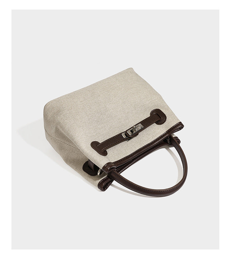 Small structured beige canvas top-handle bag with dark brown leather-look trim, silver turn-lock hardware, and detachable