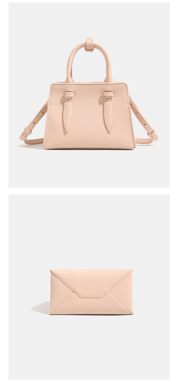 Small structured trapezoid top-handle bag in pebbled matte finish with decorative strap tabs, twin knotted handles, and