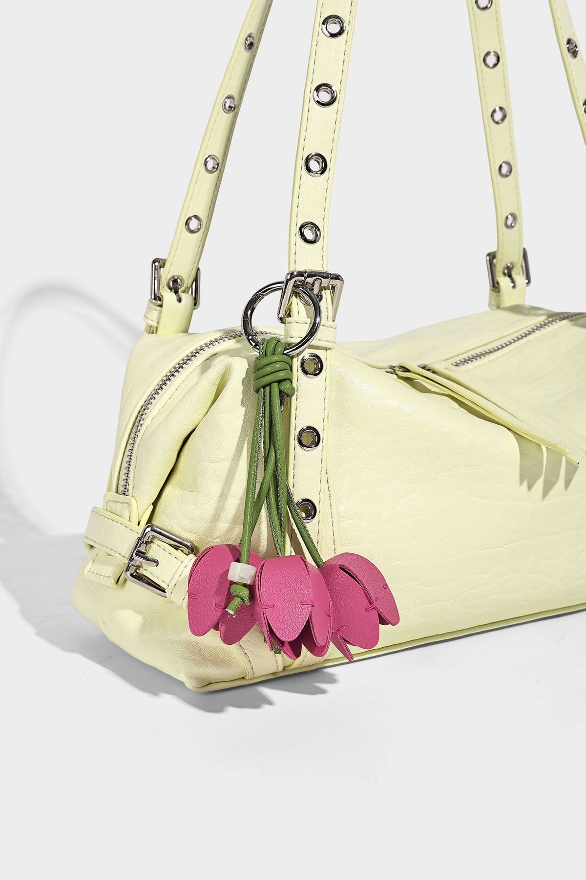 Pale yellow leather-look barrel bag with silver grommet-studded shoulder straps, top zip closure, and pink tulip floral