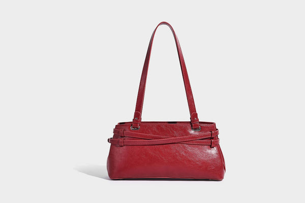 Structured glossy leather-look shoulder bag with wraparound belt straps, silver-tone hardware, and dangling star charm