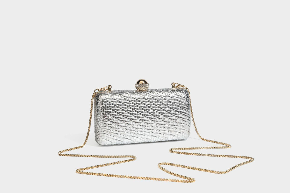 Small structured metallic woven-texture box clutch bag with jeweled kiss-lock dome clasp and slim gold chain strap, detail