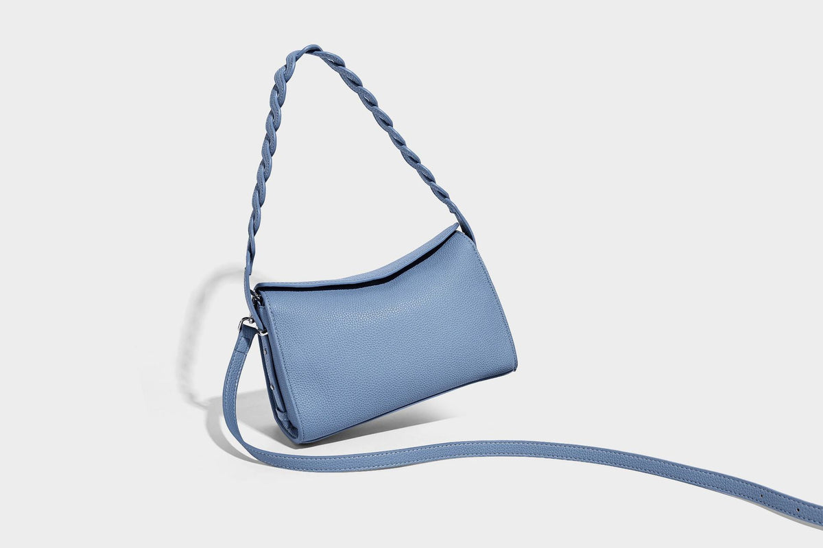 Small structured pebbled-finish shoulder bag with braided top handle, detachable crossbody strap, floral tassel charm, and