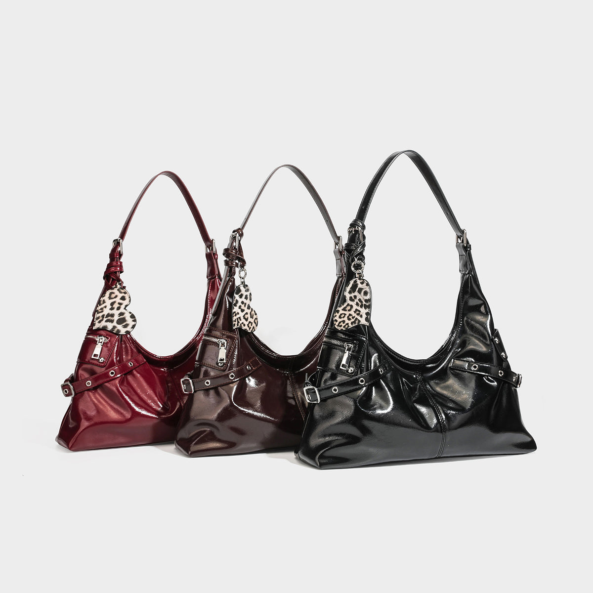 Glossy dark brown slouchy hobo shoulder bag with silver grommet strap detail, front zip pocket, and leopard-print heart