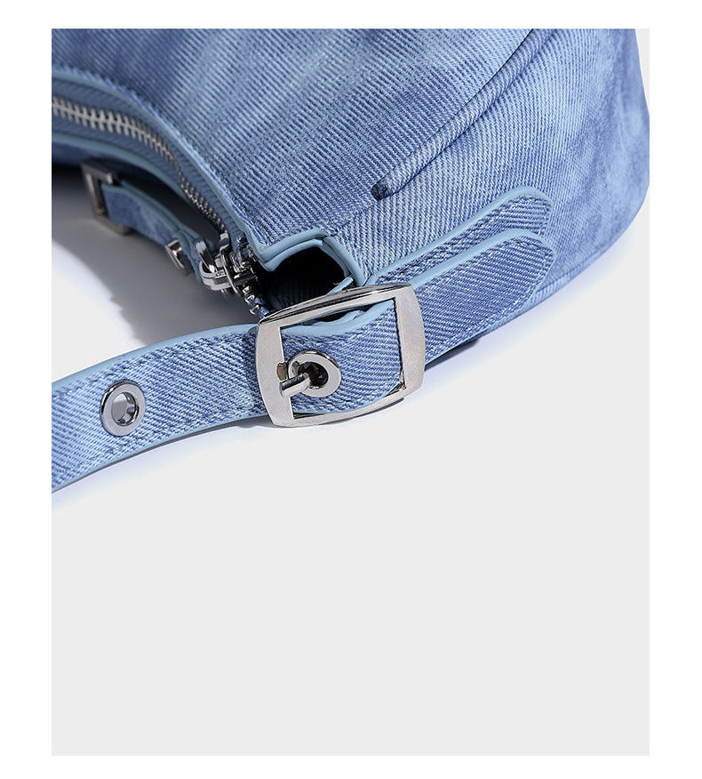 Crescent shoulder bag in washed blue denim-look PU with stacked buckle straps, front zip pocket, and silver-tone hardware