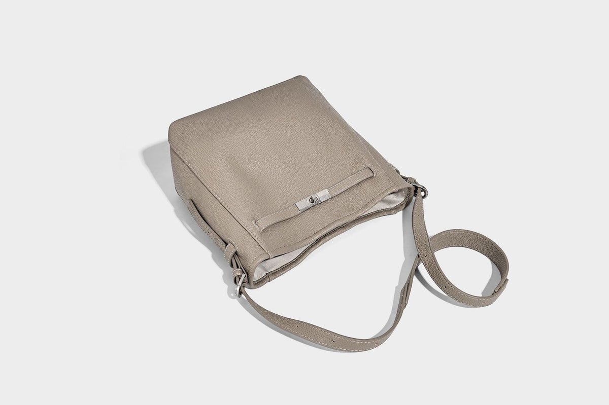Soft-structured pebbled bucket shoulder bag with front turn-lock strap detail, adjustable strap, and hanging floral tassel