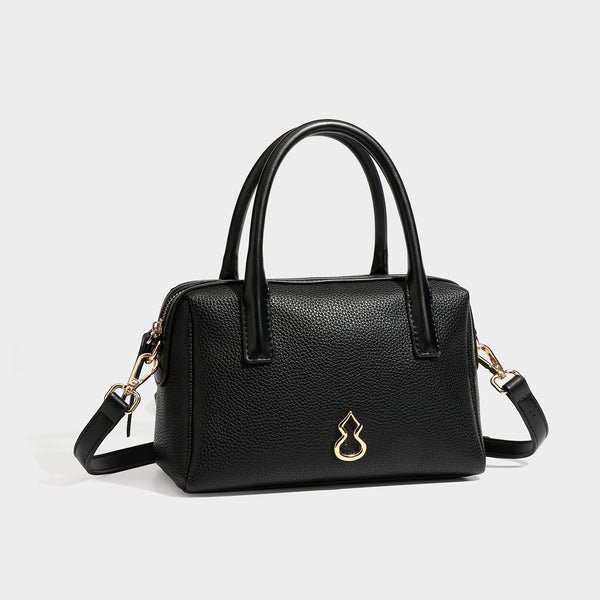 Small structured pillow satchel bag with pebbled leather-look finish, dual rolled top handles, gold-tone gourd emblem, and