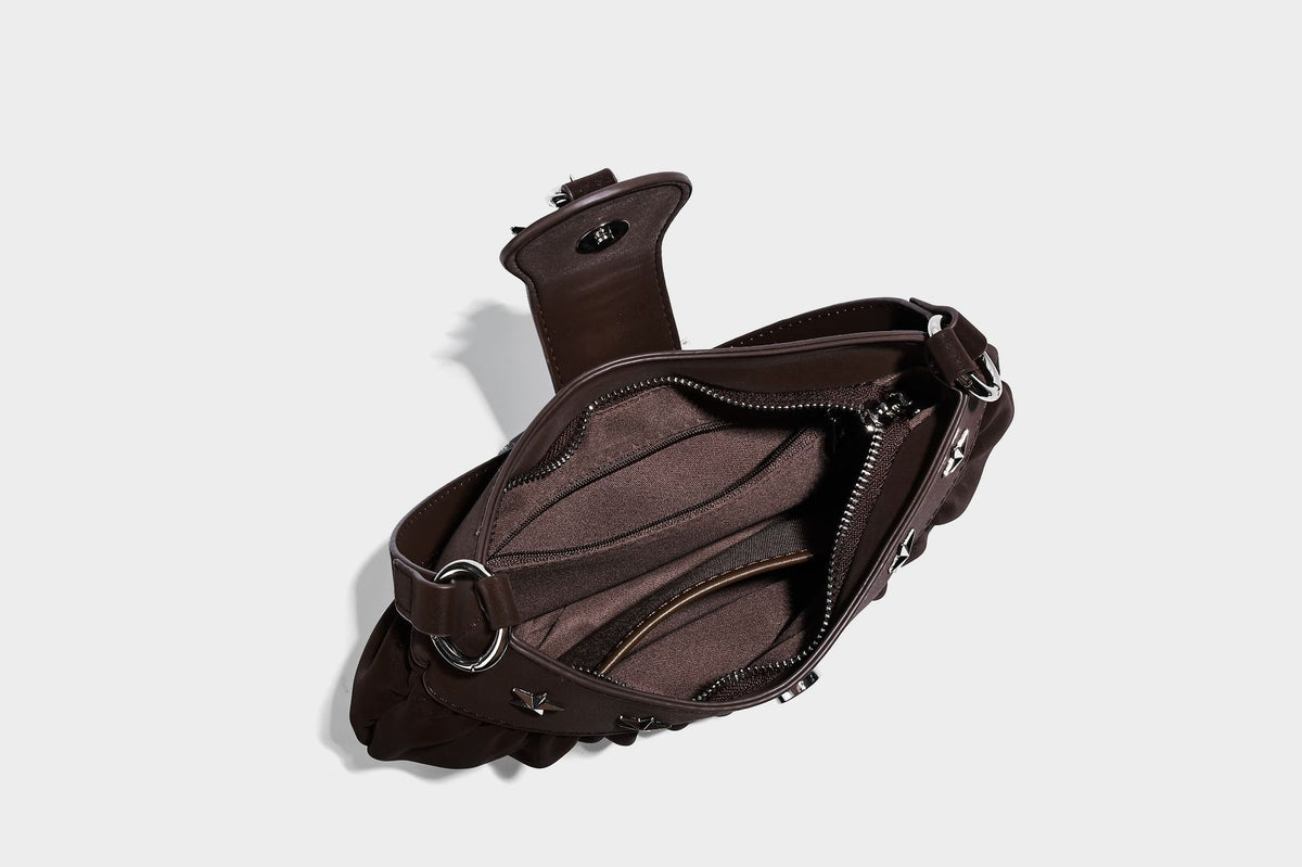 Ruched shoulder bag with curved flap, silver star studs, dangling starfish charm, and adjustable crossbody strap, detail view