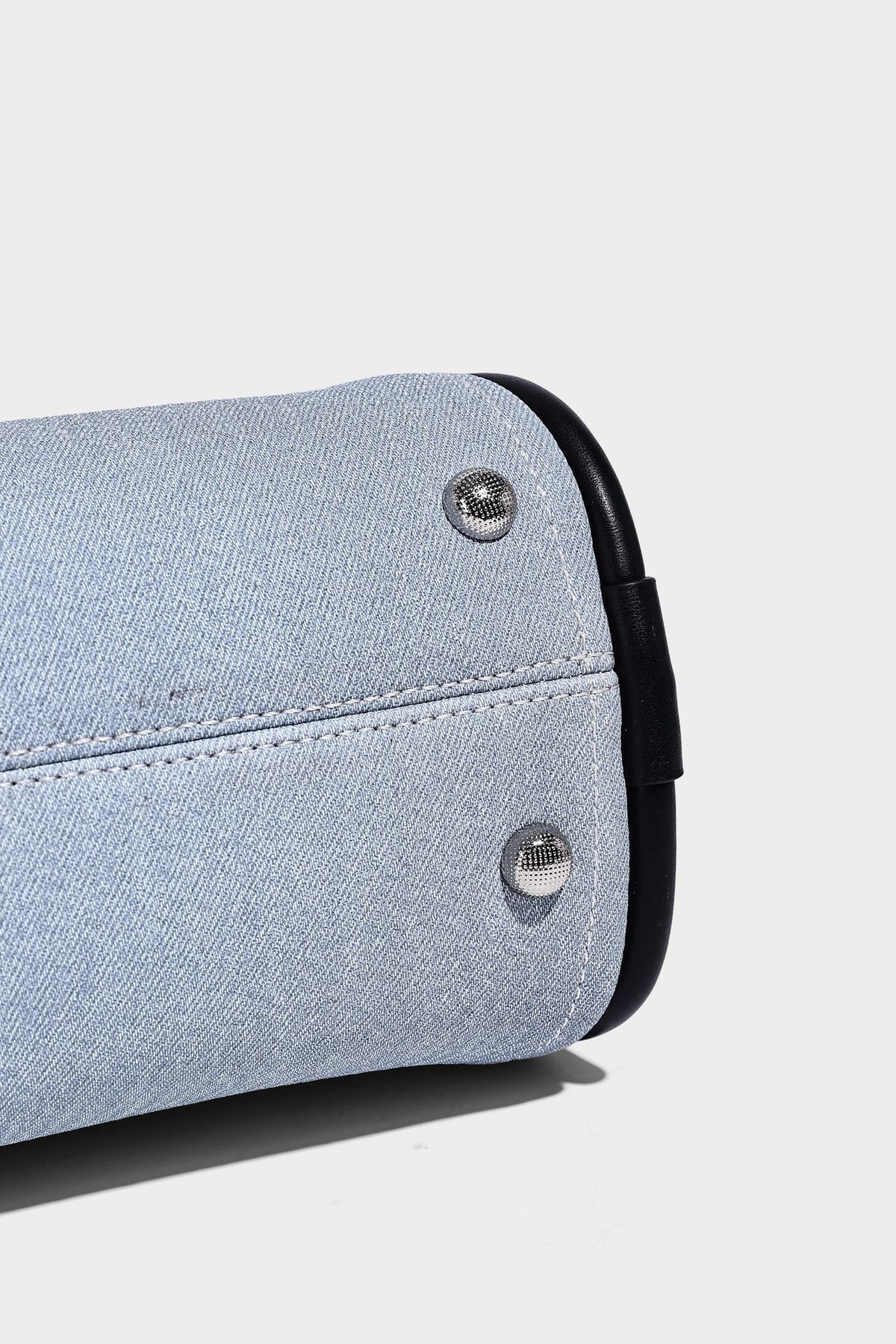 Light blue denim trapezoid tote bag with black leather-look trim, knotted top handles, detachable crossbody strap, front