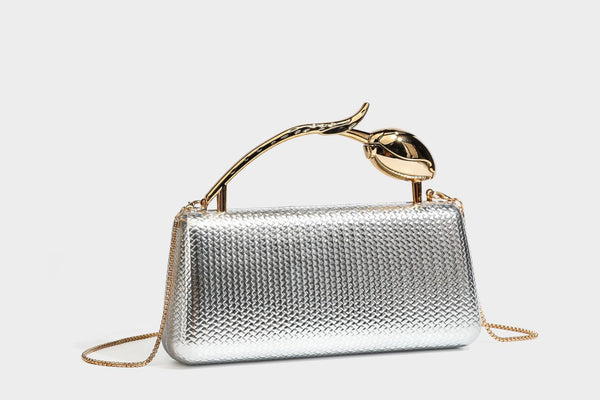 Structured rectangular metallic woven clutch bag with sculptural gold-tone leaf top handle and detachable chain strap, detail