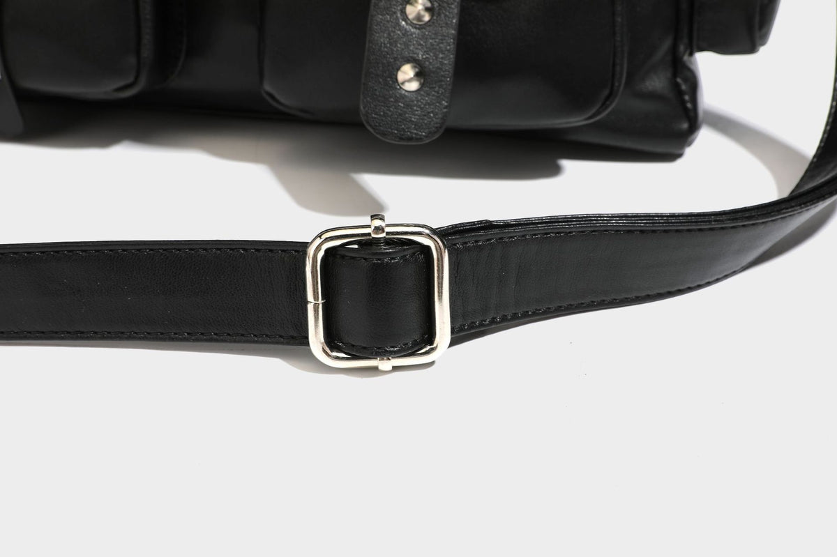 Black leather-look tote bag with silver pyramid studs on handles and front panel, multiple flap and zip exterior pockets