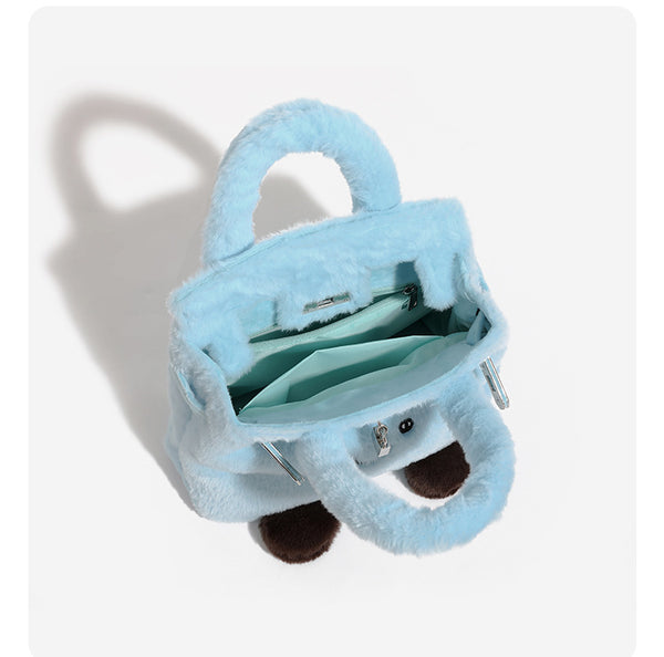 Ice-blue plush faux-fur Kelly-style convertible bag with embroidered smiling face, dark pom-pom feet, silver-tone clasp