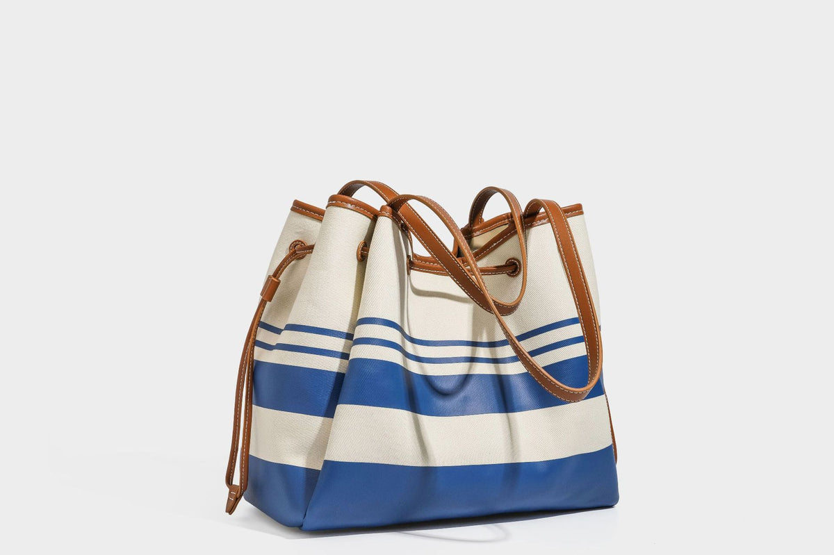 Large cream and navy striped canvas bucket tote bag with tan leather-look trim, drawstring closure, and double shoulder