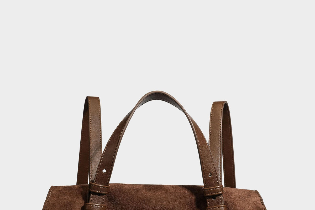 Structured suede-look convertible backpack handbag with flap closure and gold-tone emblem hardware in chocolate brown, detail