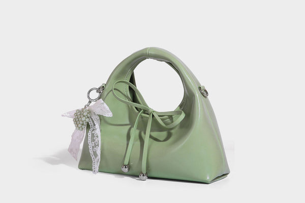 Kleine kuppelförmige Henkeltasche in glänzender Lederoptik mit Kordelzugverschluss, weißem Spitzen-Schleifenanhänger und silberfarbenen Metallbeschlägen