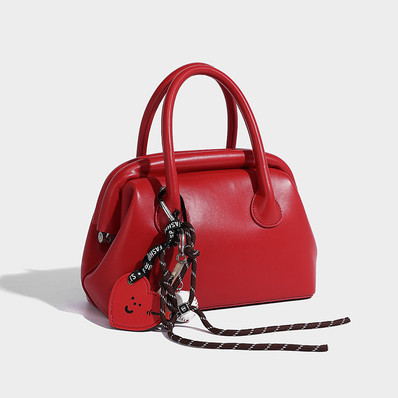 Small structured shell top-handle bag in red with heart charm and braided cord detail, smooth leather-look finish, detail