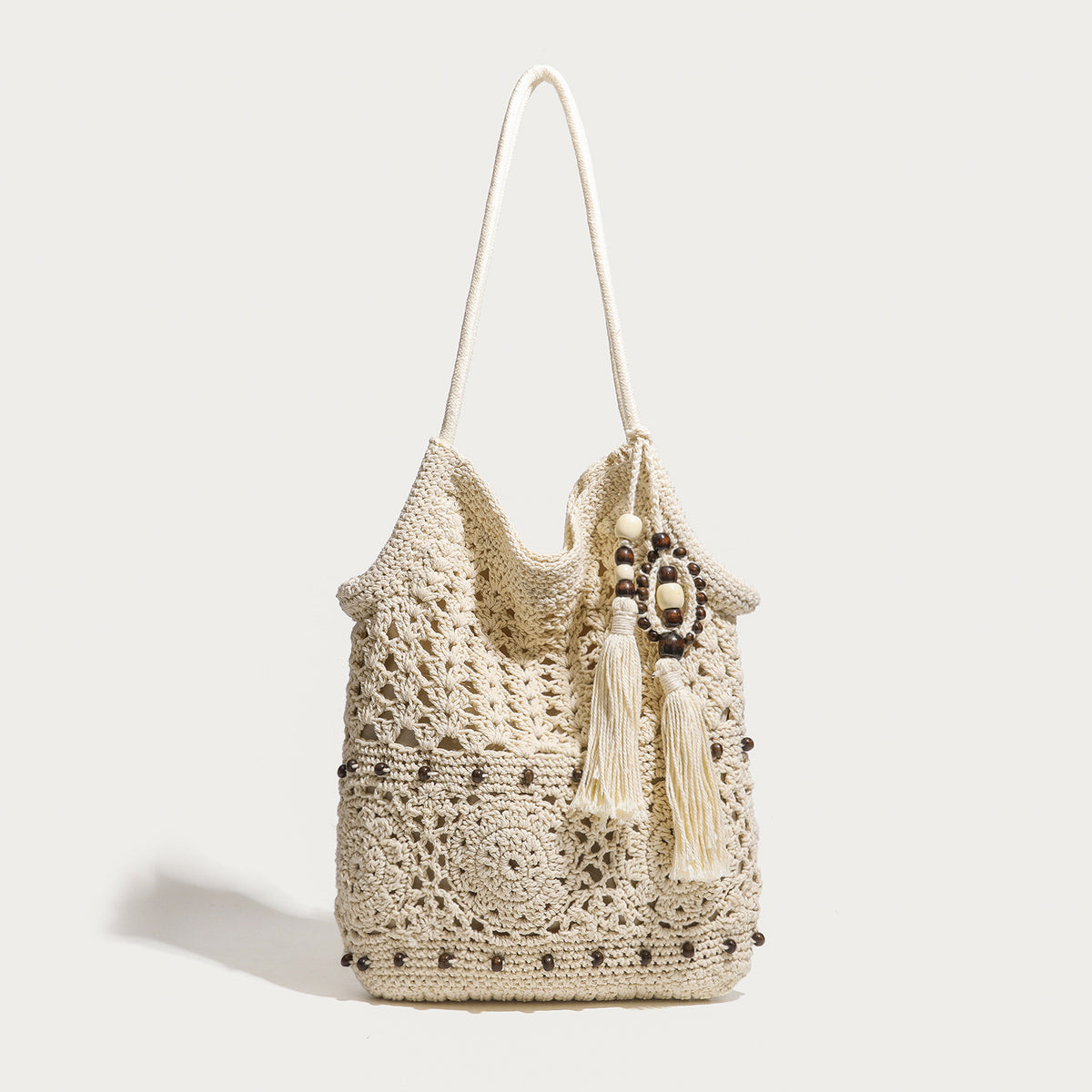 Cream openwork floral crochet tote bag with tassel and wooden bead charm and long rope shoulder straps, front view