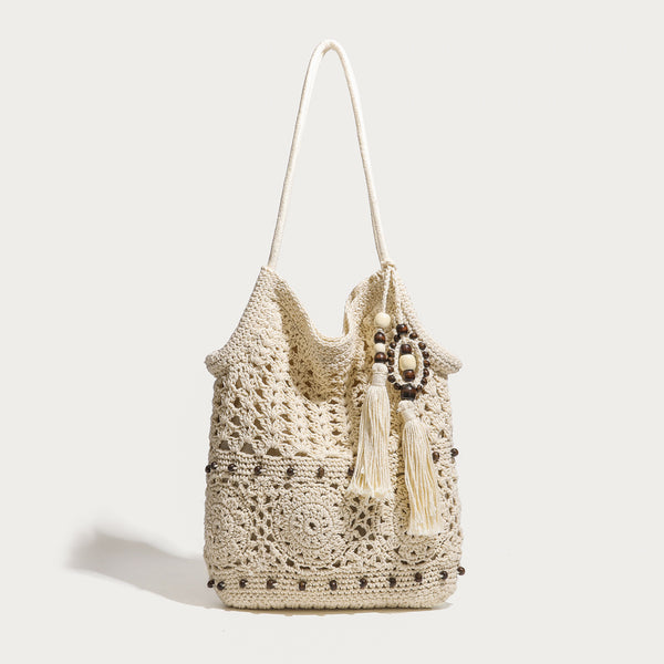 Cream openwork floral crochet tote bag with tassel and wooden bead charm and long rope shoulder straps, front view