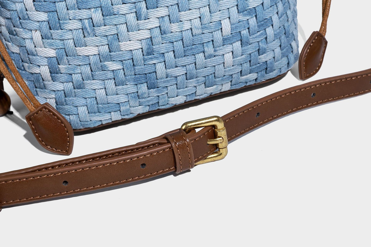 Small light blue woven bucket bag with brown leather-look trim, braided top handle, brass-tone ring hardware, drawstring