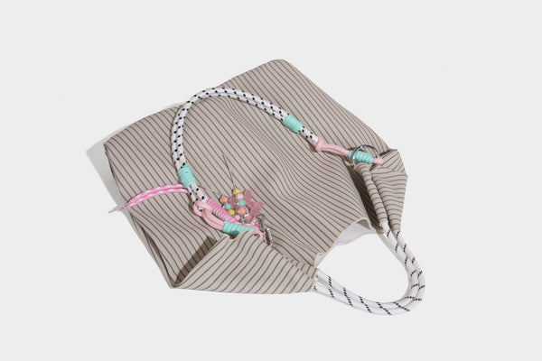 Slouchy pinstripe tote bag with braided rope handles, metal ring hardware, and colorful knotted rope charm, detail view 24