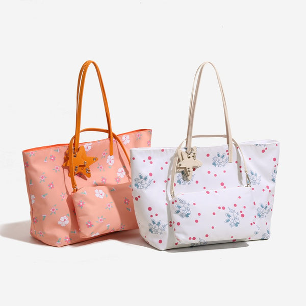 Large reversible floral print tote bag with slim shoulder straps, star charm hardware, and matching zip pouch, front view
