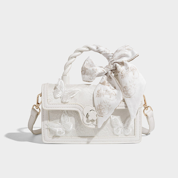 Small structured white flap bag with butterfly embroidery, flower-shaped turn-lock clasp, braided top handle with scarf bow