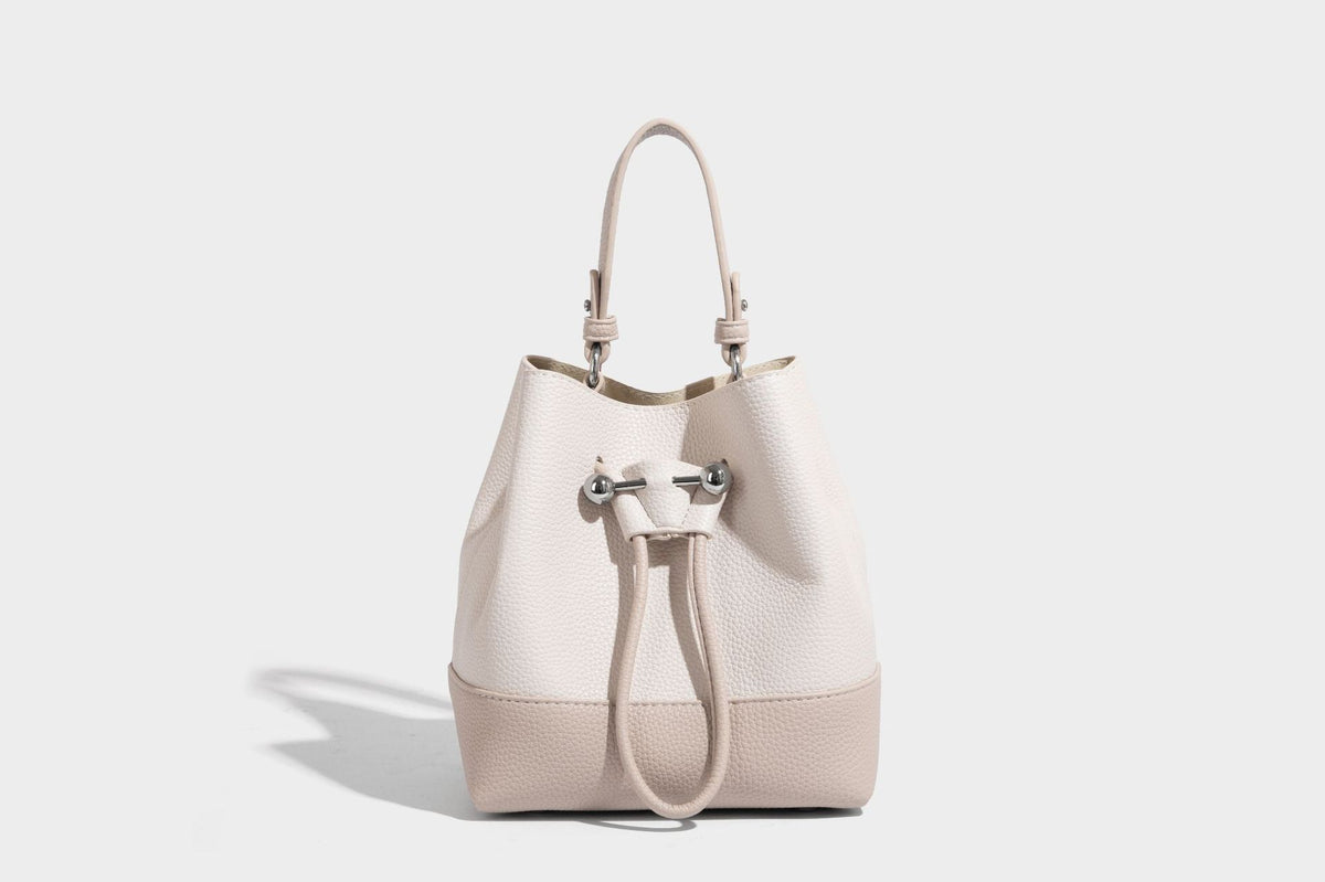 Small two-tone pebbled drawstring bucket bag with tan contrast base, metal toggle hardware, short top handle, and detachable