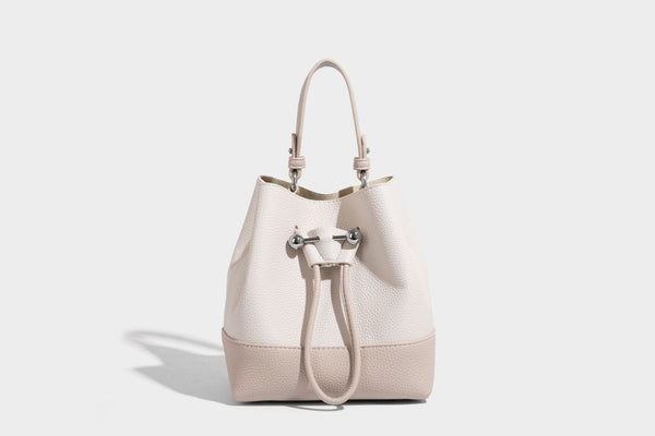 Small two-tone pebbled drawstring bucket bag with tan contrast base, metal toggle hardware, short top handle, and detachable