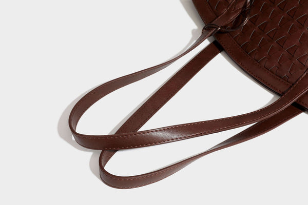 Large leather-look tote bag with geometric woven emboss, double shoulder straps, and round woven cord charm in brown, detail
