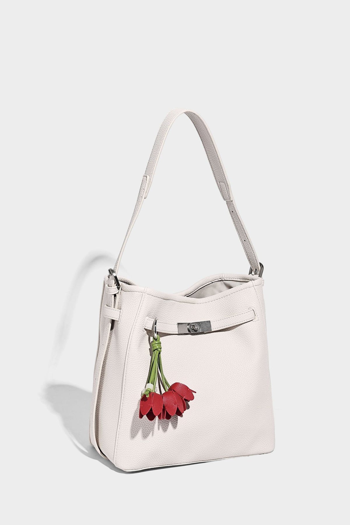 Soft-structured pebbled bucket shoulder bag with front turn-lock strap detail, adjustable strap, and hanging floral tassel