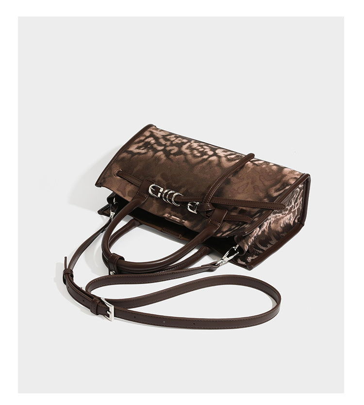 Structured leopard-print tote bag with glossy satin-like finish, dual rounded top handles, silver buckle-and-ring front