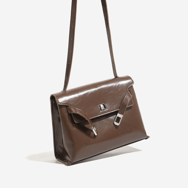 Structured trapezoidal flap satchel bag with silver-tone turn-lock clasp, decorative front strap tabs, gusseted sides, and