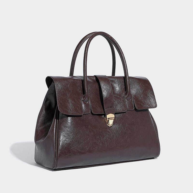 Structured glossy leather-look satchel tote with flap-over closure, center strap, gold-tone turnlock, and dual top handles