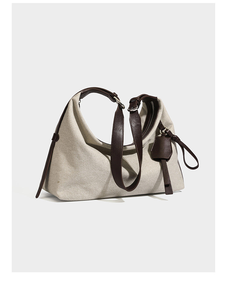 Cream canvas hobo shoulder bag with dark brown leather-look trim, zip-top closure, adjustable strap, and silver-tone