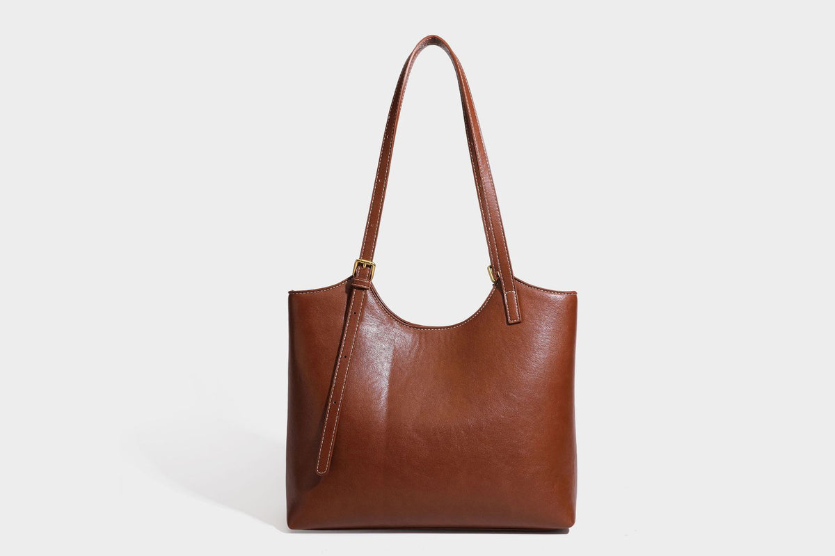 Structured smooth leather-look tote bag with long shoulder strap, gold-tone hardware, and hanging tassel-coin charm, detail