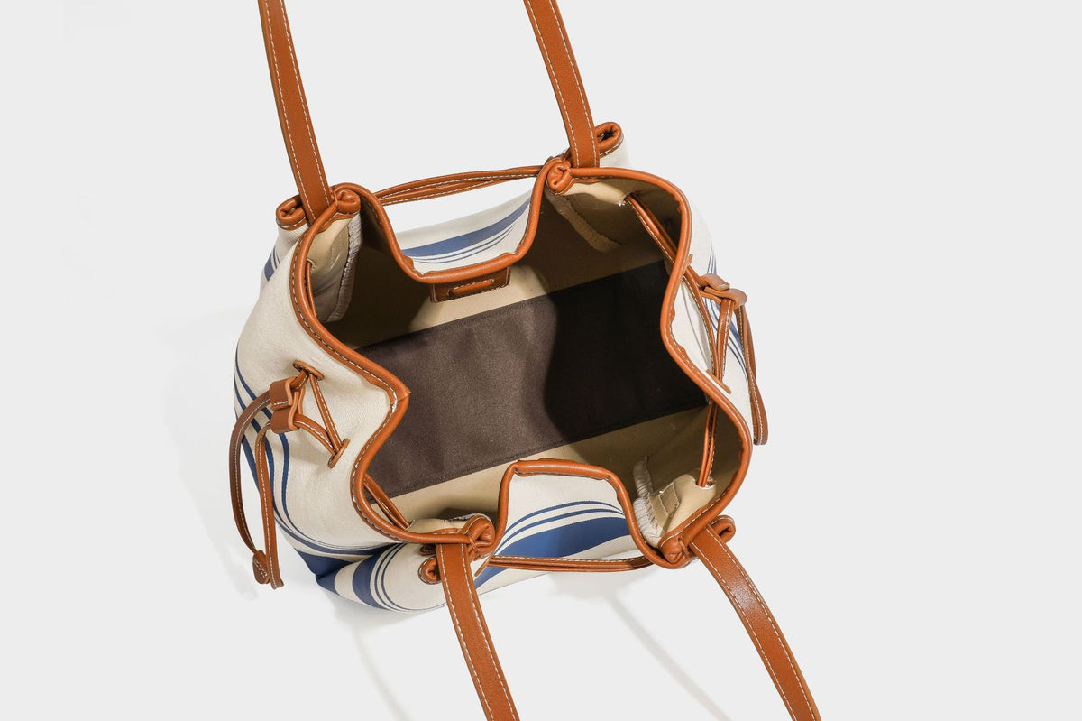 Large cream and navy striped canvas bucket tote bag with tan leather-look trim, drawstring closure, and double shoulder