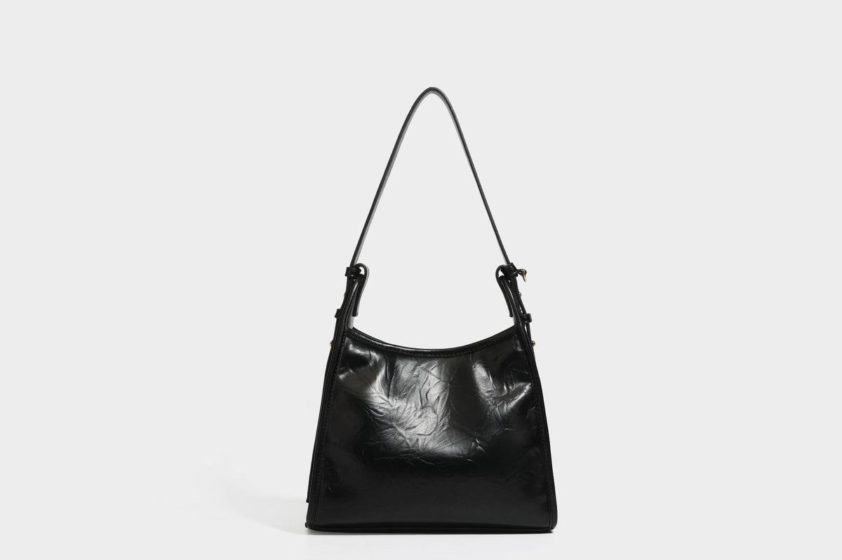Strukturierte, trapezförmige Schultertasche aus glänzender, geknautscht wirkender Lederoptik mit goldfarbenen Beschlägen auf der Vorderseite und langem, verstellbarem