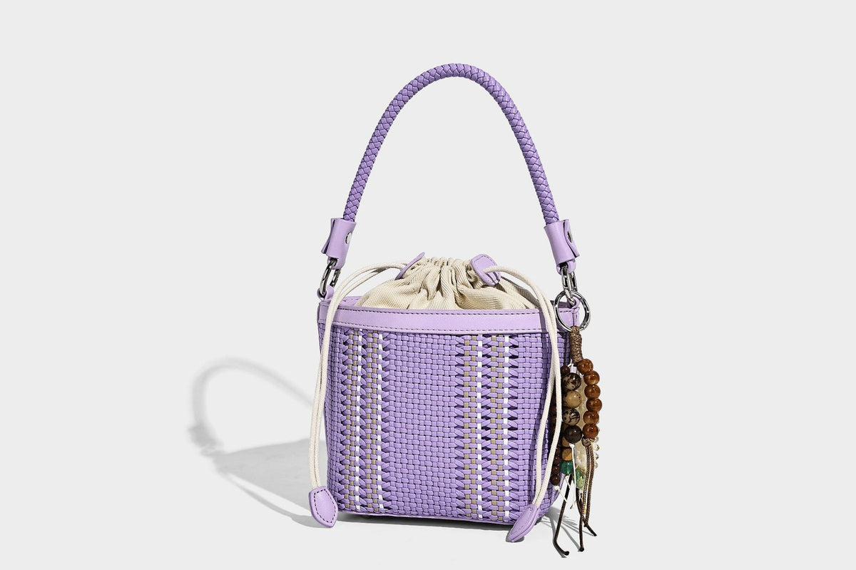 Small woven bucket bag with drawstring top, braided handle, detachable crossbody strap, and silver-tone ring hardware, detail
