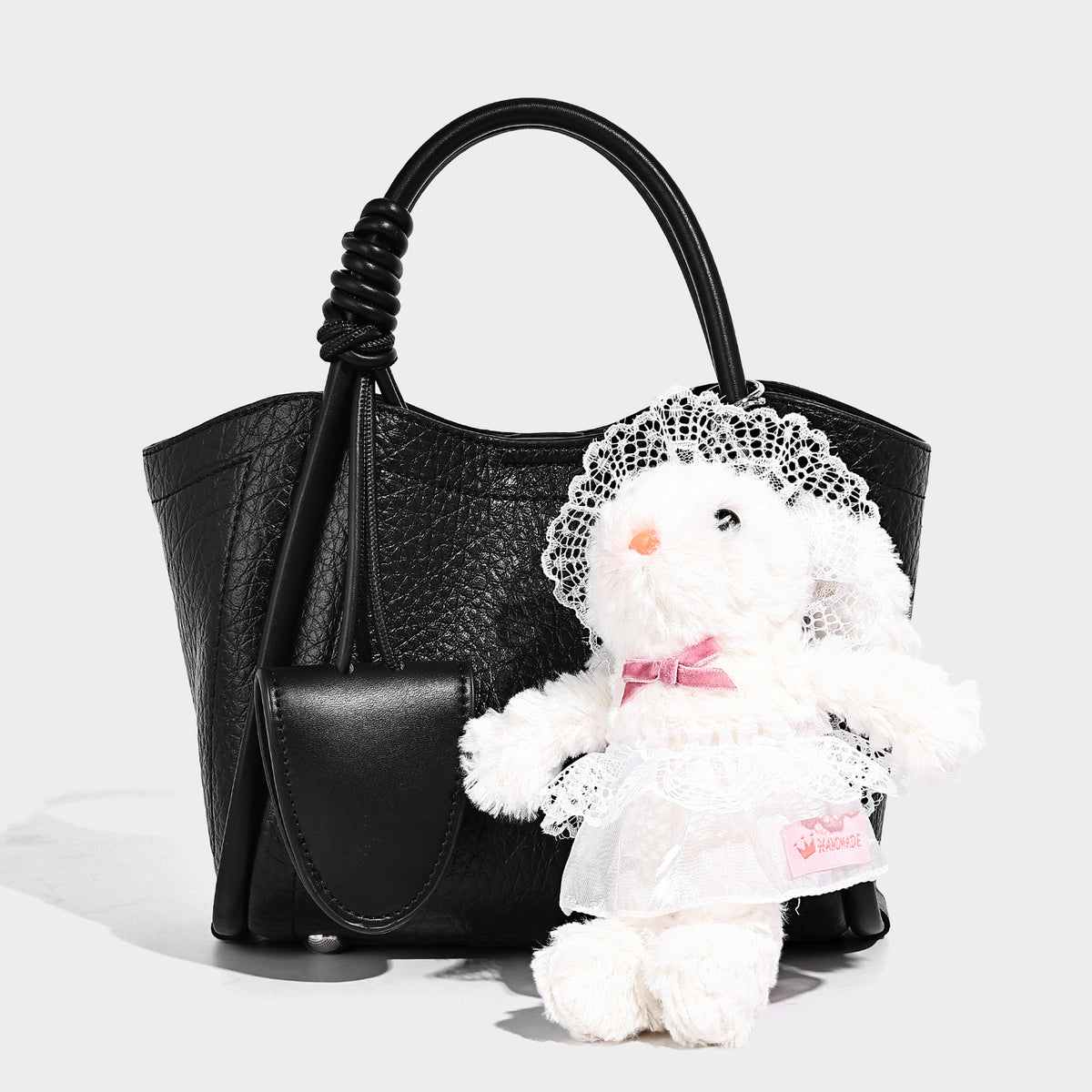 Structured mini tote bag in pebbled leather-look finish with knotted top handles, front flap pocket, and detachable shoulder