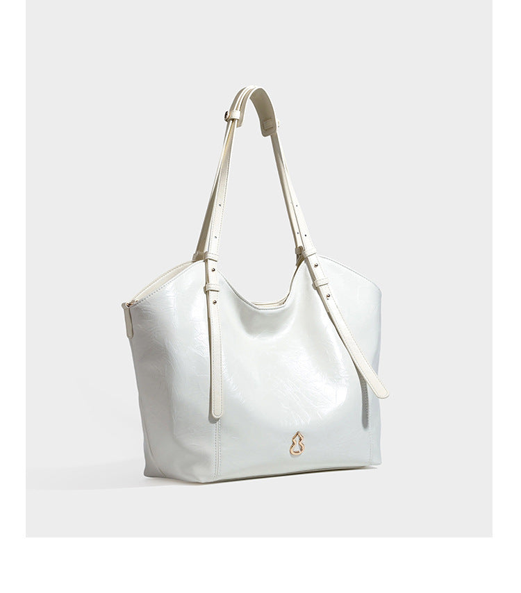 Große, glänzende Tote-Bag aus schwarzem Lederimitat mit geknitterter Optik, lässig fallender Trapezsilhouette, zwei Schulterriemen und goldfarbenen