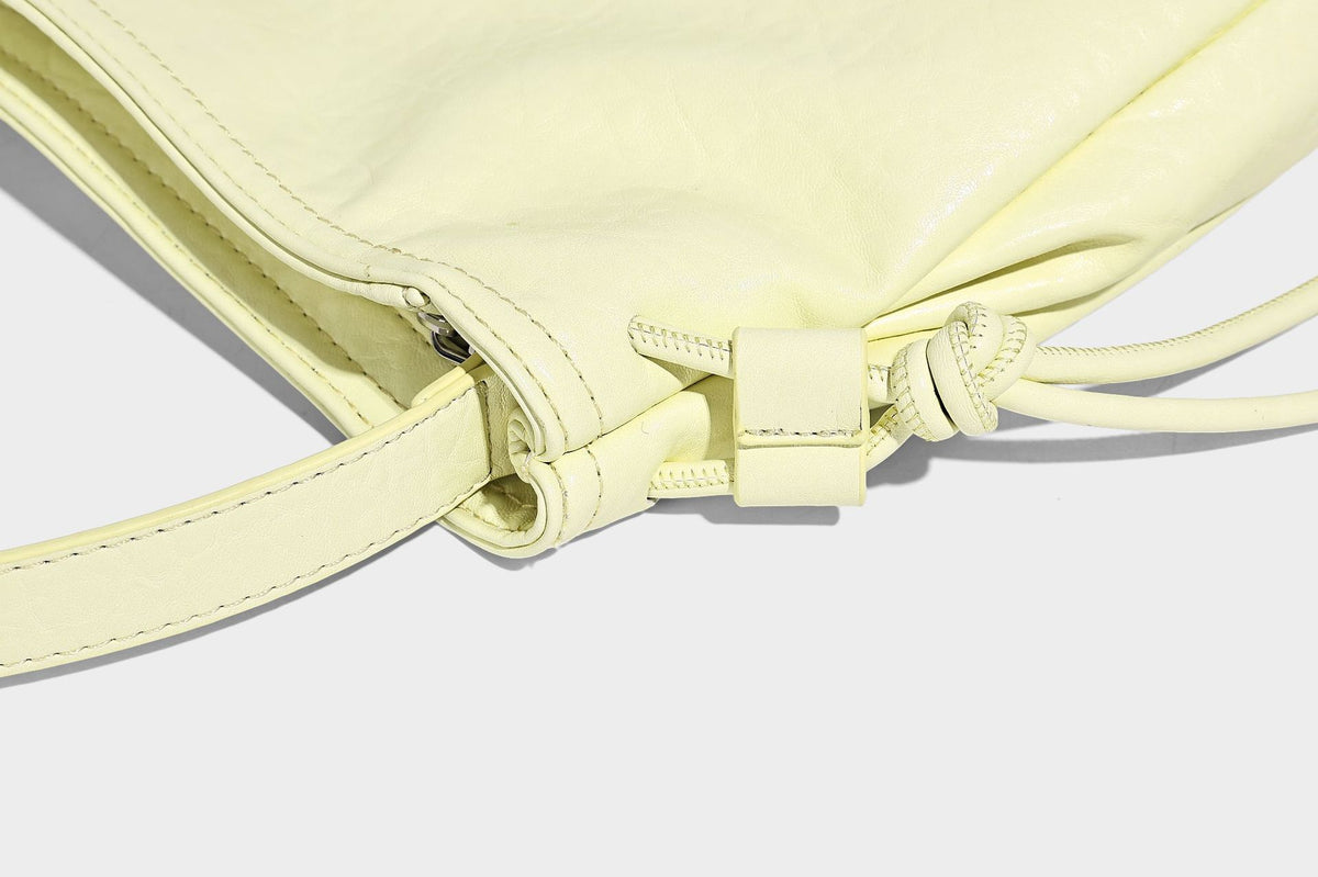 Slouchy hobo shoulder bag in pale yellow with slim strap, drawstring bead closure, and pink tulip floral charm, detail view